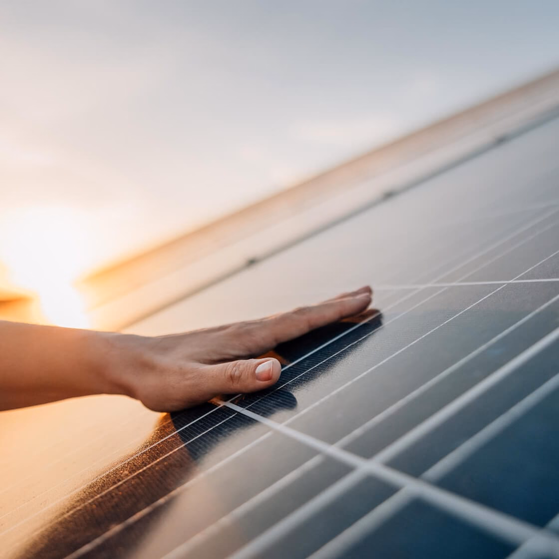 Hand op een zonnepaneel in het licht van de ondergaande zon